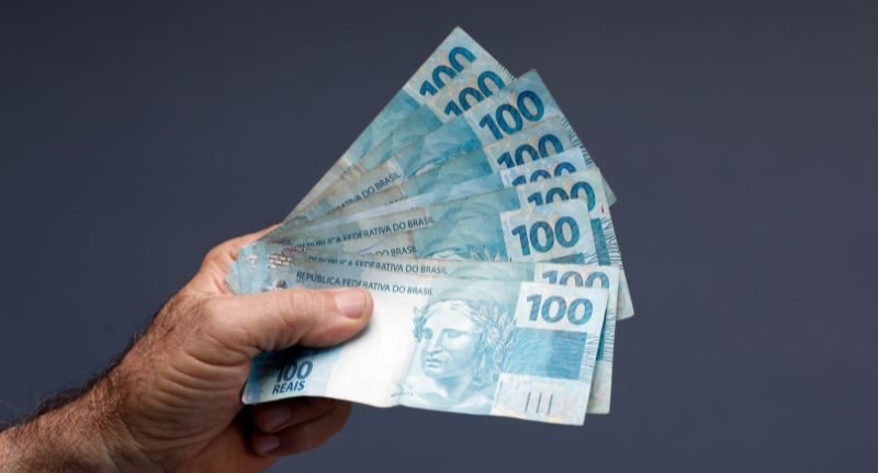 Mão masculina segurando o dinheiro do 13º salário de sua empresa